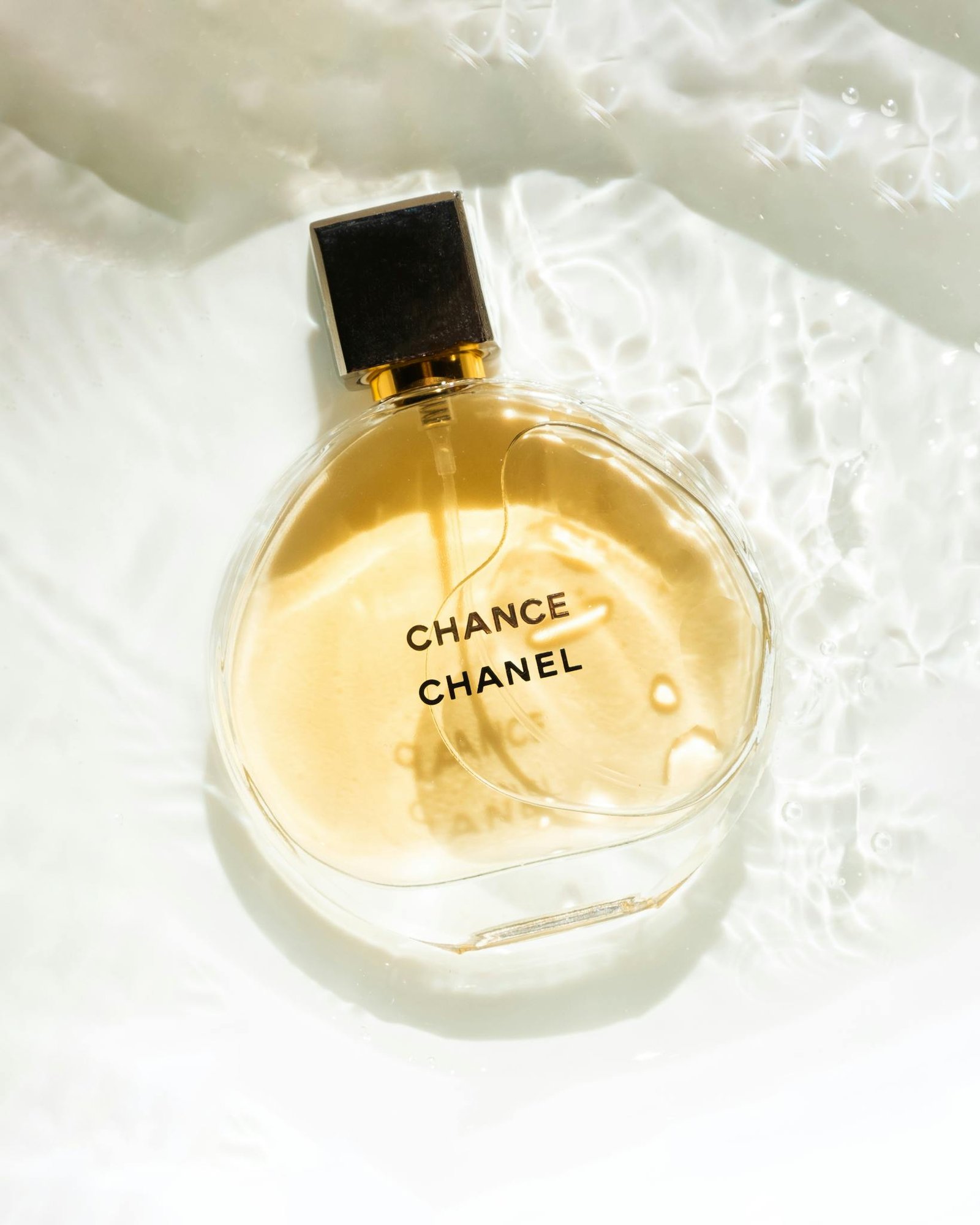 Chanel Chance perfume bottle with water reflections on a white background, showcasing elegance and luxury.